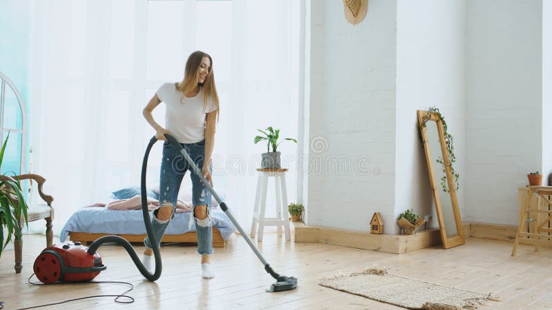 Young woman having fun cleaning house with vacuum cleaner dancing and singing at home