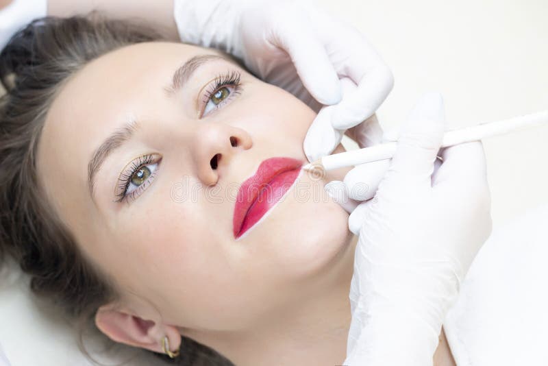 Young woman having permanent makeup on her lips at the beauticians salon
