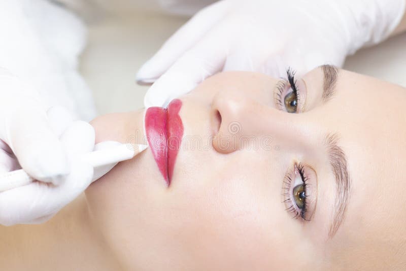Young woman having permanent makeup on her lips at the beauticians salon. Permanent Makeup Tattoo.