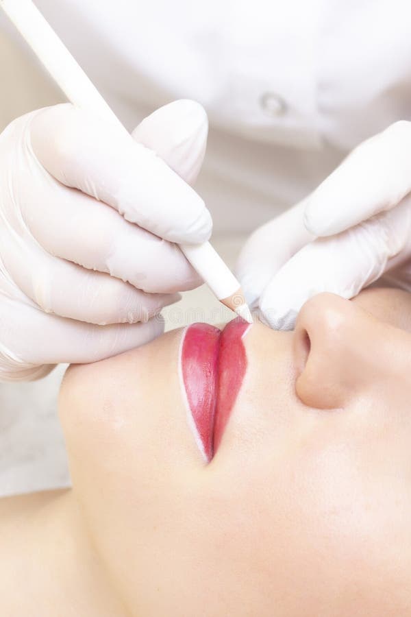 Young woman having permanent makeup on her lips at the beauticians salon.