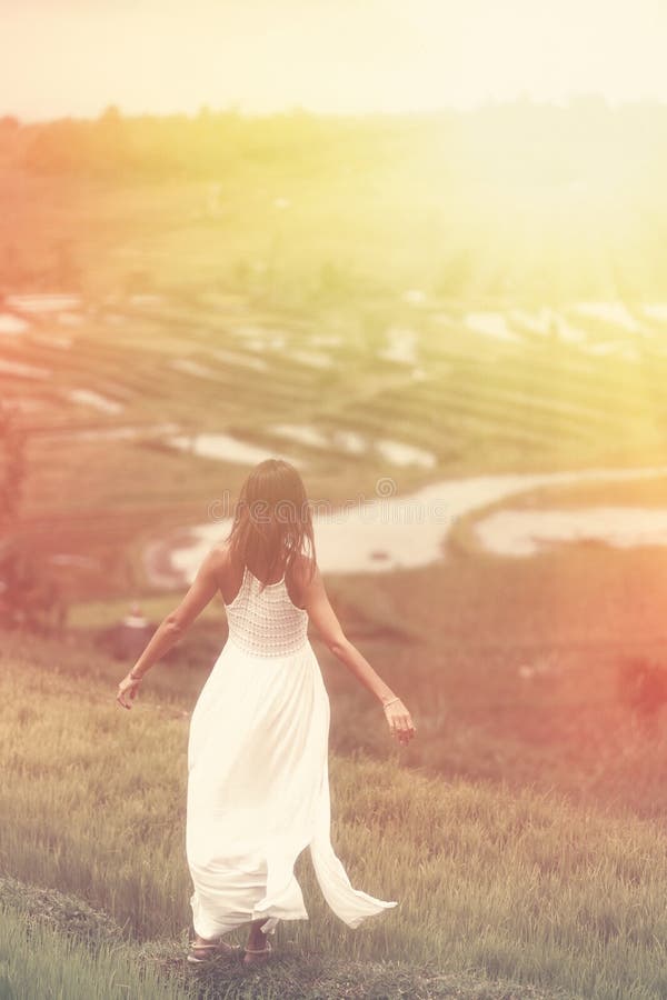 A young woman with her arms outstretched posing standing on a hill. In the background are rice fields. Tint and light from the top stock photos A young woman with her arms outstretched posing standing on a hill. In the background are rice fields. Tint and light from the top stock photos