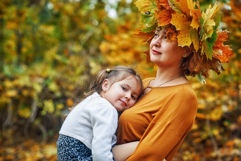A young woman with her daughter in the autumn forest . Portrait of a happy girl with her mother . stock photo A young woman with her daughter in the autumn forest . Portrait of a happy girl with her mother . stock photo