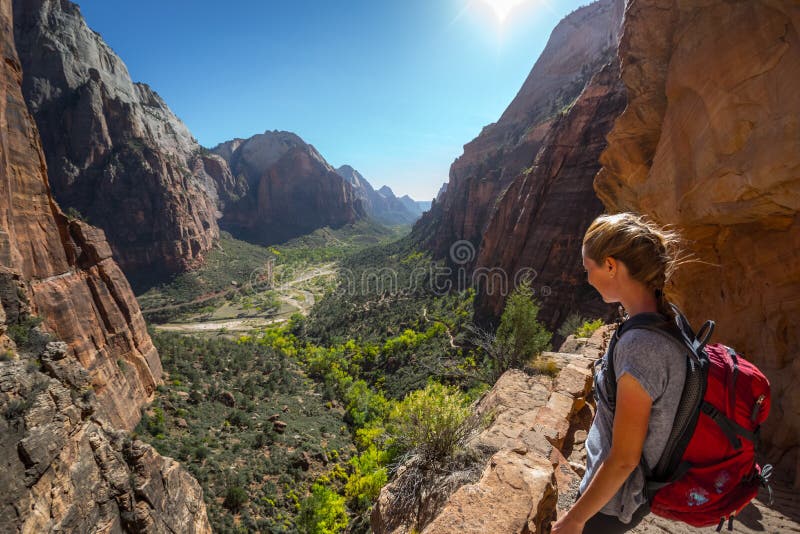 Young woman hiker with backpack stands on the edge and looks down at the valley of Zion National Park, Angels Landing trail, USA