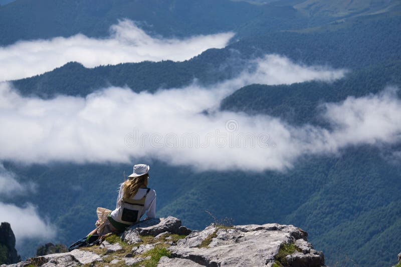Young woman in hiking gear sits on a rocky ledge, overlooking a misty mountain landscape stock images