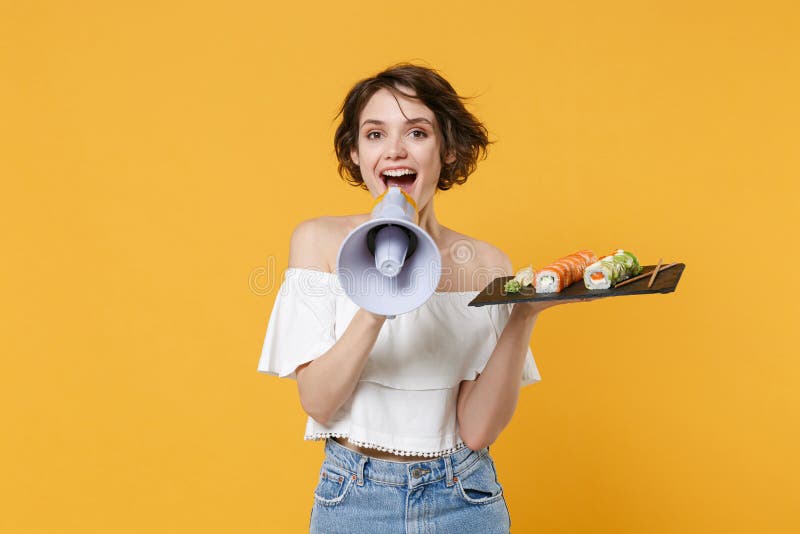 Young woman hold in hand makizushi sushi roll served on black plate japanese food scream in megaphone announces stock photo
