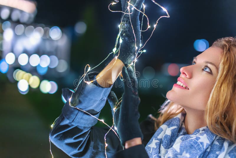 Young woman holding christmas fairy lights at night outdoors in