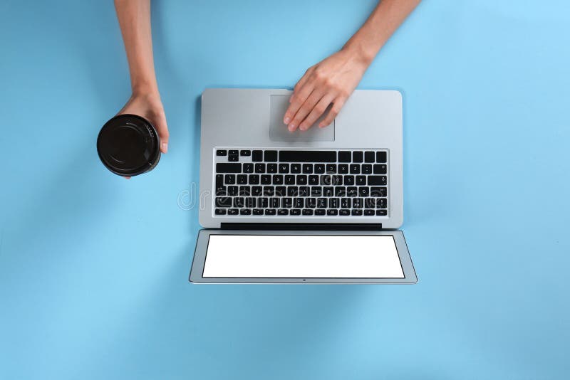 Young woman holding coffee while using laptop on light blue background, top view