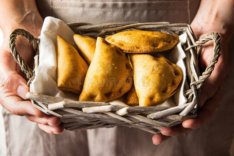 Young woman holding in hands wicker basket with freshly baked empanadas turnover pies with vegetables cheese in tomato sauce. Knfolk style. Cozy authentic atmosphere. Young woman holding in hands wicker basket with freshly baked empanadas turnover pies with vegetables cheese in tomato sauce. Knfolk style. Cozy authentic atmosphere.