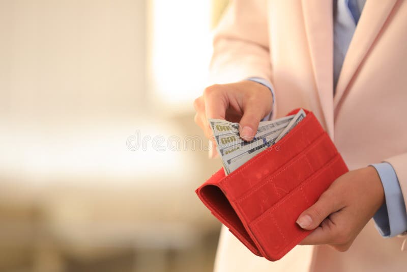 Young woman holding wallet with dollar bills on blurred background