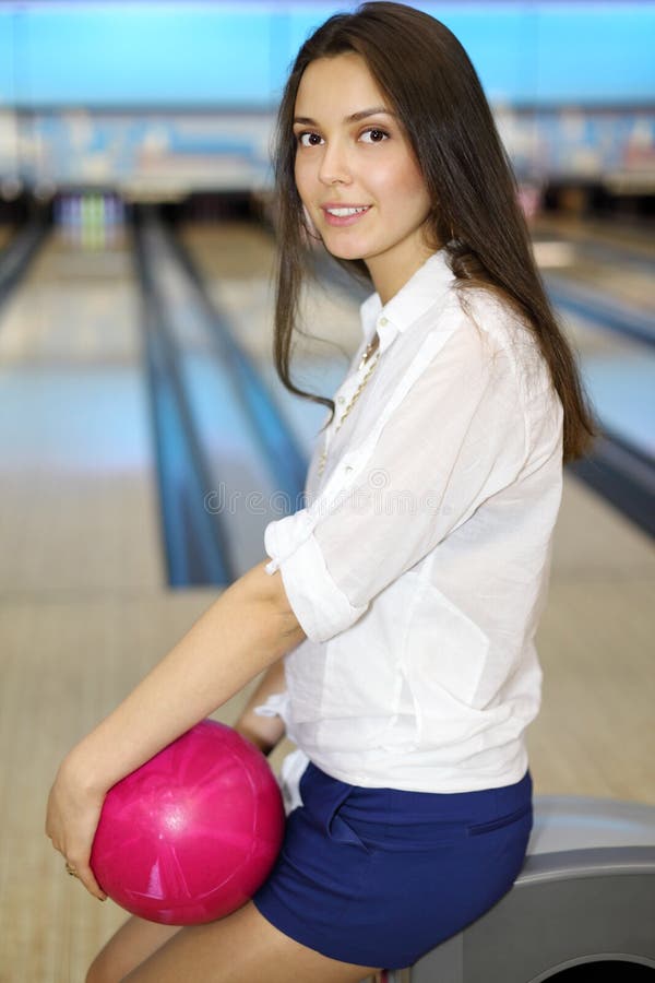 Young woman holds ball and sits in bowling club