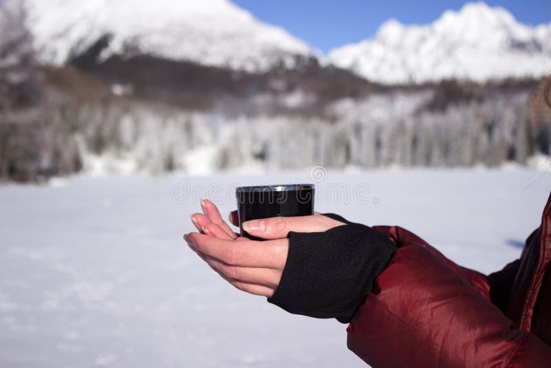 A young woman holds a cup of tea against the background of mountains in winter. Strbske Pleso Lake, Slovakia