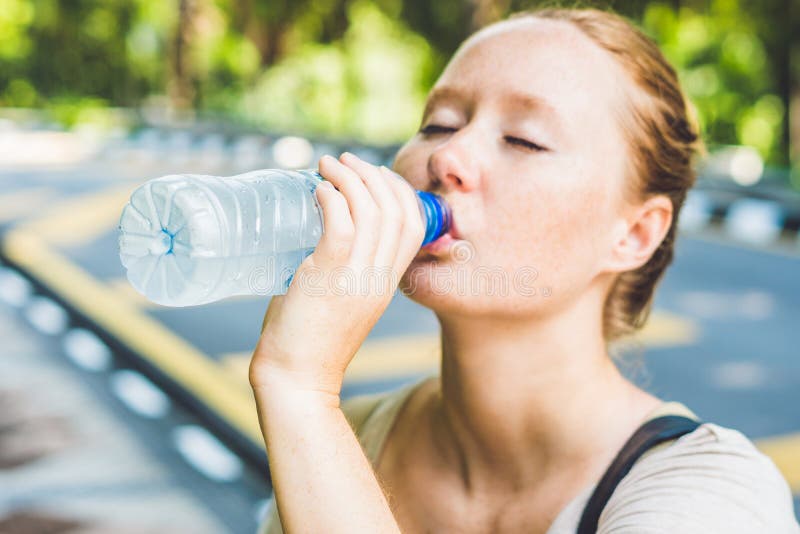 Young woman in hot weather drinks water from a bottle