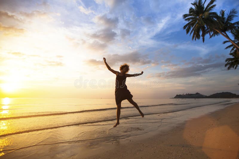 Young woman jumping on the sea coast during the amazing sunset.