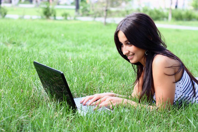 Young woman with laptop lying jn the green grass