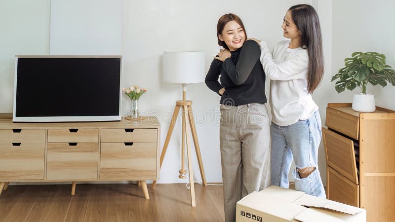 Young woman lesbian couple moving to a new home and girlfriend massaging her shoulders from the lift the box for move to stock image