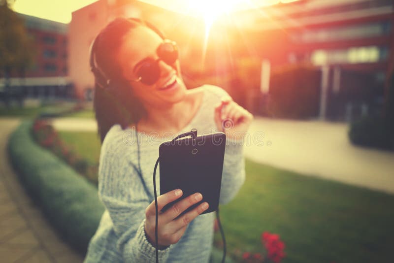 Young woman listening music by tablet and headphones in sunset