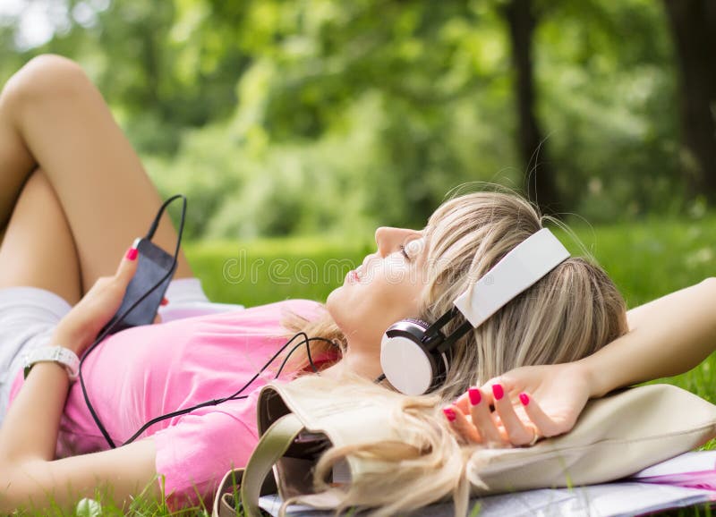 Young woman listening to music while laying down on grass