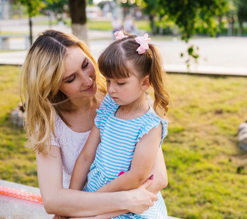 A young woman and a little girl are sitting on a bench in the park.Similarity and kinship