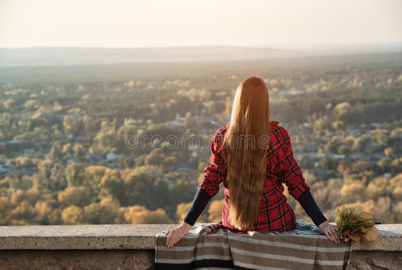 Young woman with long hair sits on a hill overlooking the village. Back view stock photos Young woman with long hair sits on a hill overlooking the village. Back view stock photos