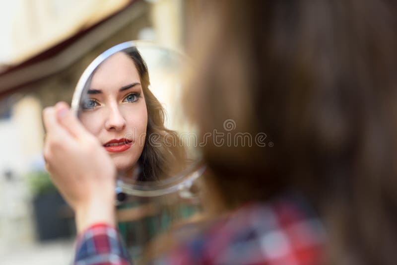 Young woman looking at herself in a little mirror