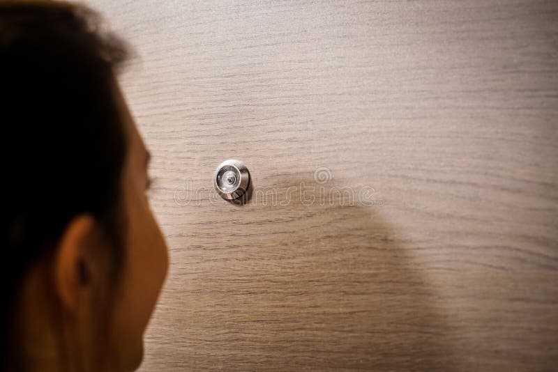 Young woman looking out through the peephole of her front door.