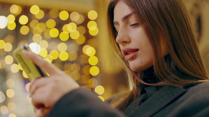 Young woman with loose hair chats on smartphone sitting in expensive restaurant