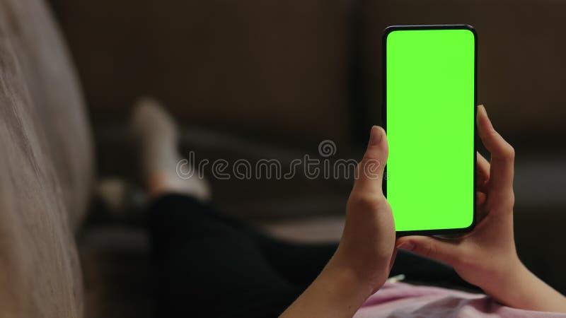 Young woman lying on a couch and using smartphone with vertical green screen stock footage