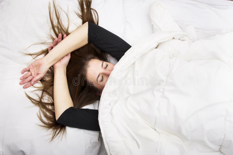 Young woman is lying in her bed with closed eyes, smiling under her blanket after a restful sleep. royalty free stock photography Young woman is lying in her bed with closed eyes, smiling under her blanket after a restful sleep. royalty free stock photography
