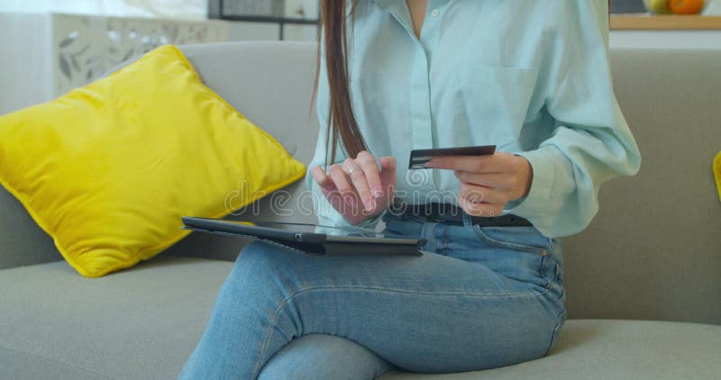Young woman is making online payment holding bank card using modern PC Tablet at home sitting on sofa and smiling royalty free stock images Young woman is making online payment holding bank card using modern PC Tablet at home sitting on sofa and smiling royalty free stock images