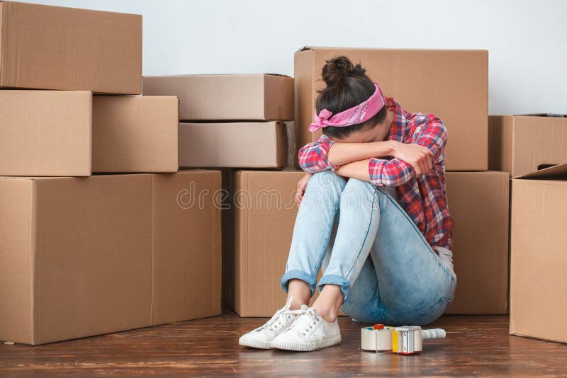 Young woman moving to new place sitting on floor face down crying exhausted. Young woman moving to new place sitting on floor face down crying exhausted