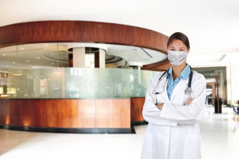 Young woman nurse or doctor wearing surgical mask and Lab Coat with arms crossed and Stethoscope draped around her neck, in