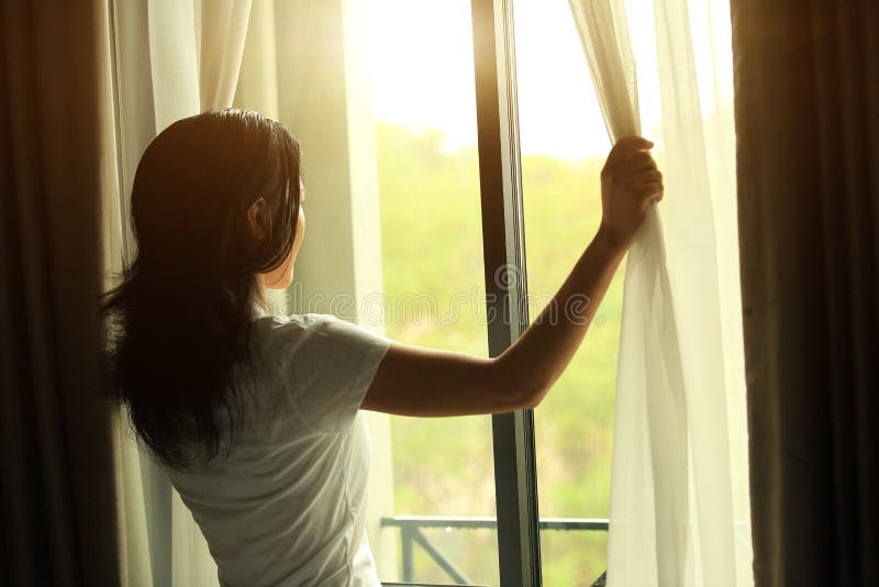 Young woman open window and curtains with sunshine morning