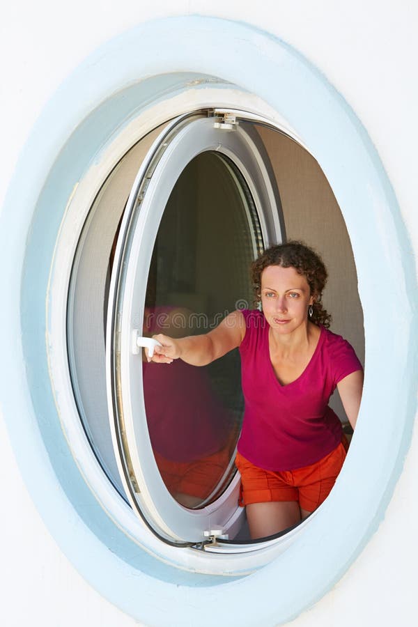 Young woman opens window made as porthole