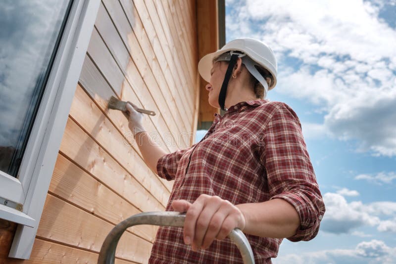 A young woman paints the outside wall of a new wooden house