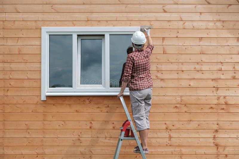 A young woman paints the outside wall of a new wooden house