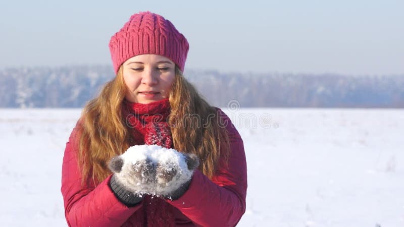 Young woman in pink clothes blowing on snow