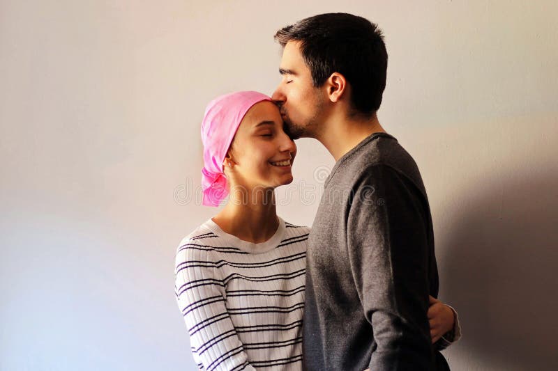 Young woman with a pink scarf next to her husband while he kisses her forehead. Concept of Support for Breast Cancer royalty free stock image Young woman with a pink scarf next to her husband while he kisses her forehead. Concept of Support for Breast Cancer royalty free stock image