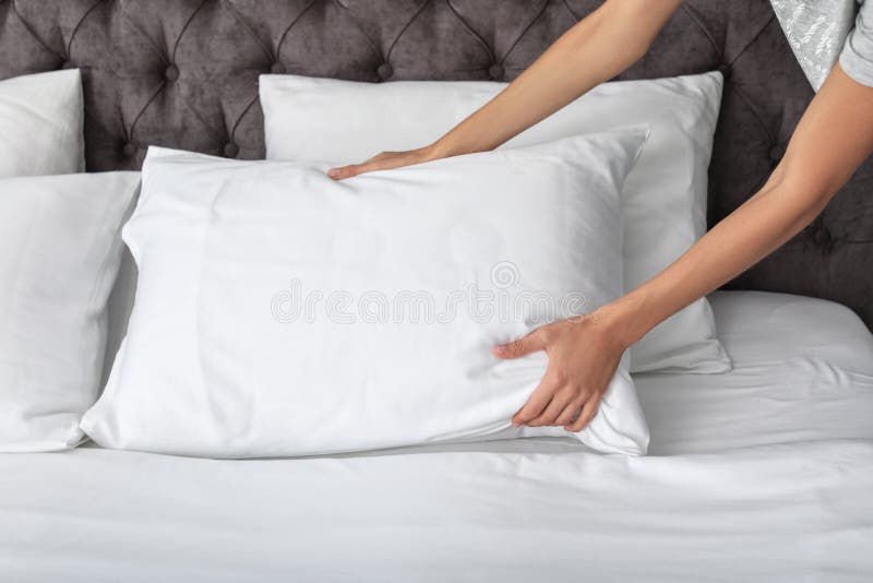 Young woman plumping white pillow on bed