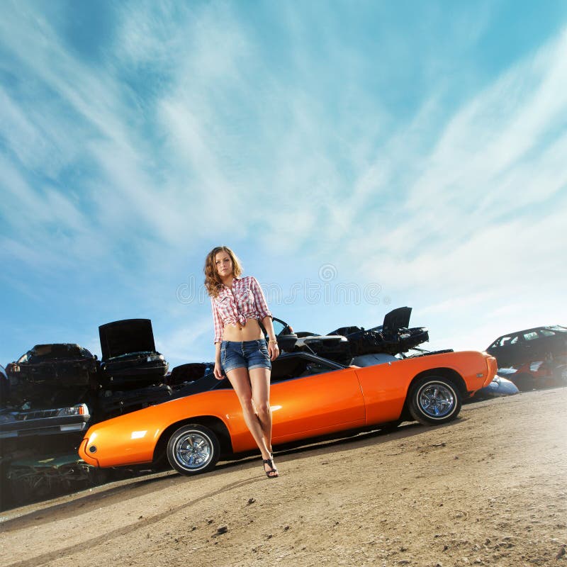 A young woman posing near an orange muscle car