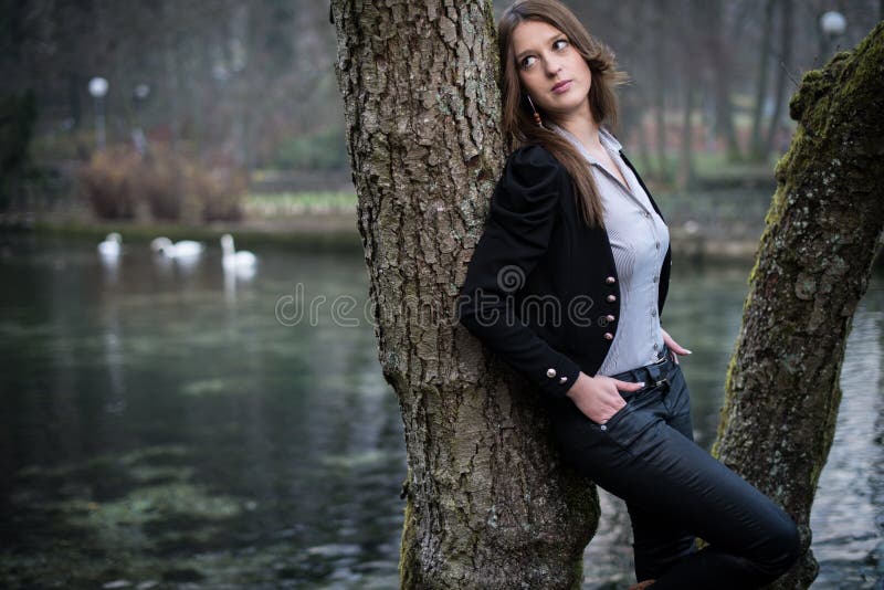 Young woman posing at the tree hands in pocket