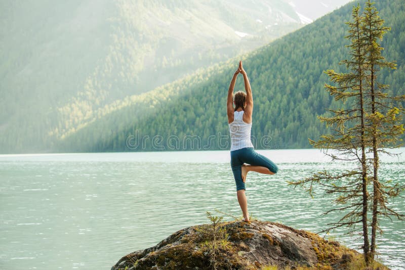 Young woman is practicing yoga at mountain lake