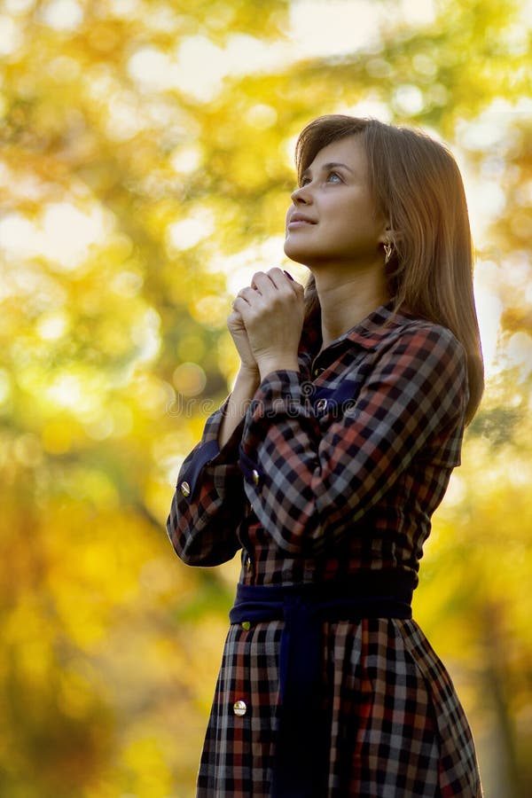 Young woman praying in nature, the girl thanks God with her hands folded at her chin, the concept of religion