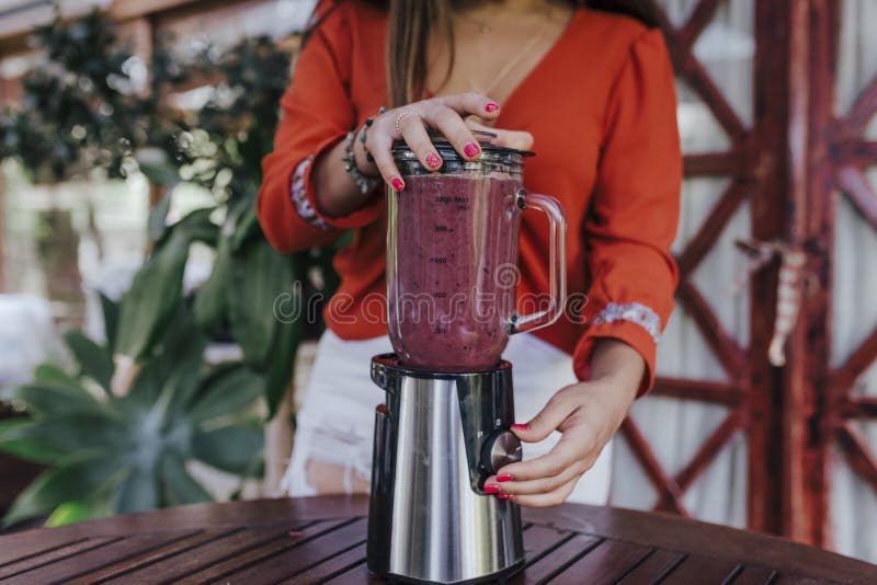 young woman preparing a healthy recipe of diverse fruits, watermelon, orange and blackberries. Using a mixer. Homemade, indoors,