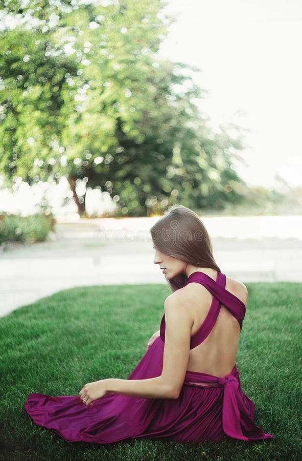 Young woman in long dress sitteng on a grass.