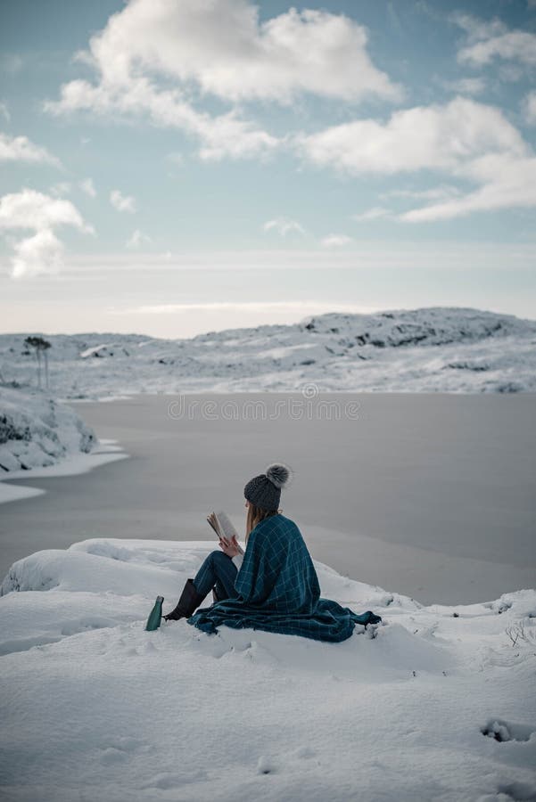 Young woman reading a book outdoors in wintertime having termobottle with tea on her side. Vertical photo. Young woman reading a book outdoors in wintertime having termobottle with tea on her side. Vertical photo.