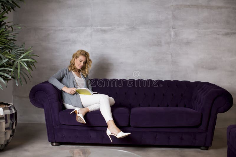 Young Woman Reading a Book and Sitting on Comfortable Sofa at Home