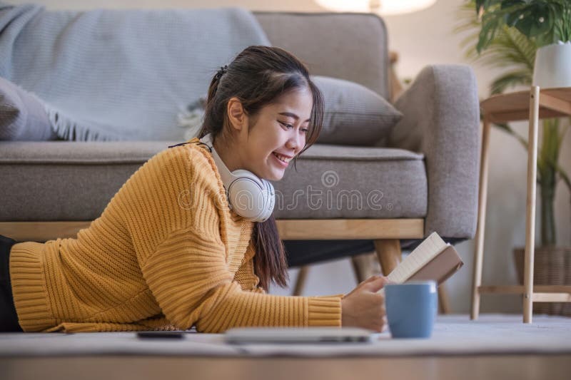 Young woman reading book on sofa in living room.