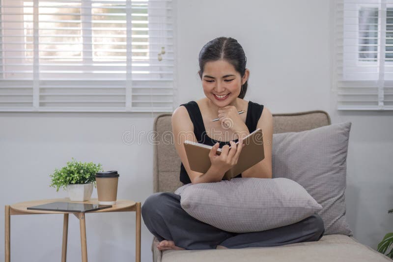 Young woman reading book on sofa in living room.