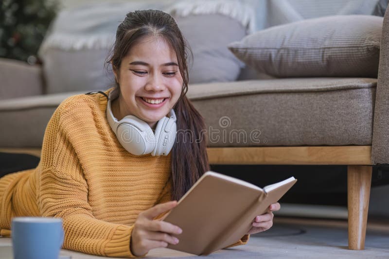 Young woman reading book on sofa in living room.