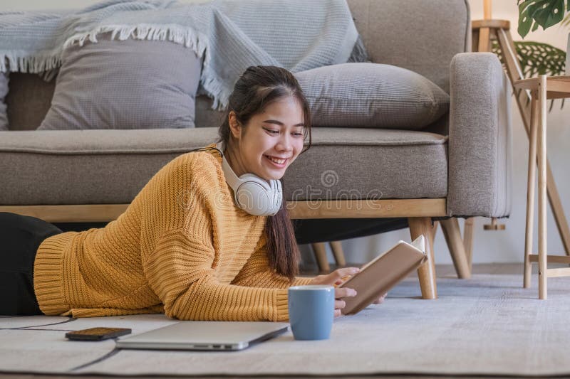Young woman reading book on sofa in living room.